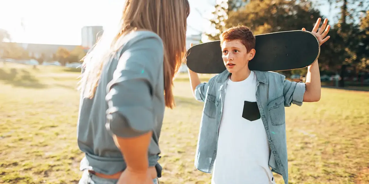 Ein Junge mit einem Skateboard über der Schulter spricht mit einer Frau. Die **Adoleszenz** ist eine spannende Zeit voller Entdeckungen.
