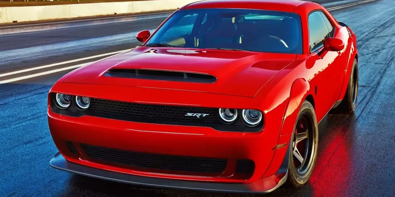 Czerwony Dodge Challenger SRT na torze wyścigowym. Potężny silnik 5.7 Hemi, choć jego spalanie może być wysokie, zapewnia niezapomniane wrażenia.