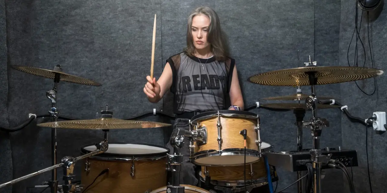 Kobieta z pałeczką w dłoni, gotowa do wygenerowania mocnych **drum beats** na zestawie perkusyjnym w studio.