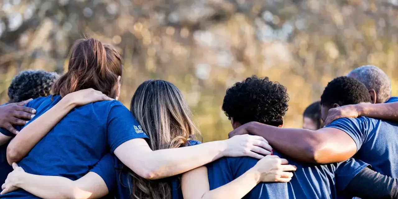 A diverse group of people in blue shirts huddle together, arms around each other, symbolizing collaboration and the strength of revenue diversification.