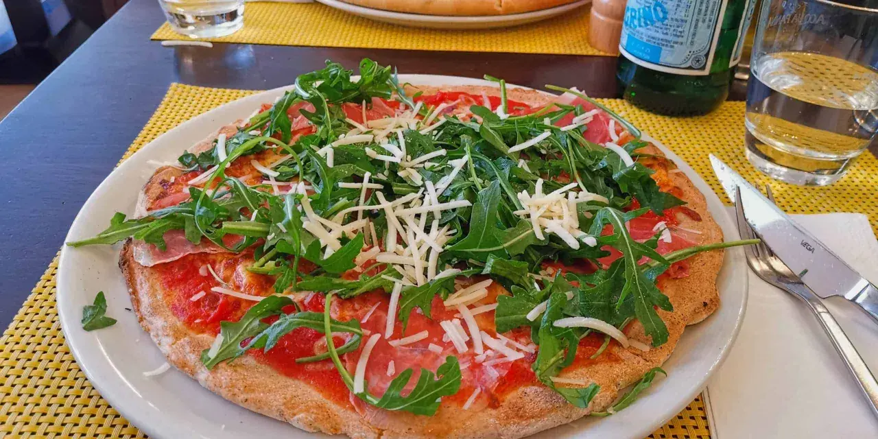 Leckere Pizza mit Rucola und Schinken auf einem Teller, ein Beispiel für glutenfreie Restaurants.