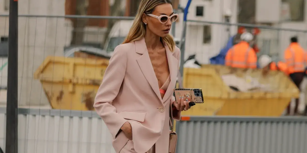 Donna con tailleur rosa, reggiseno a vista e occhiali da sole. Un look chic per ogni occasione.