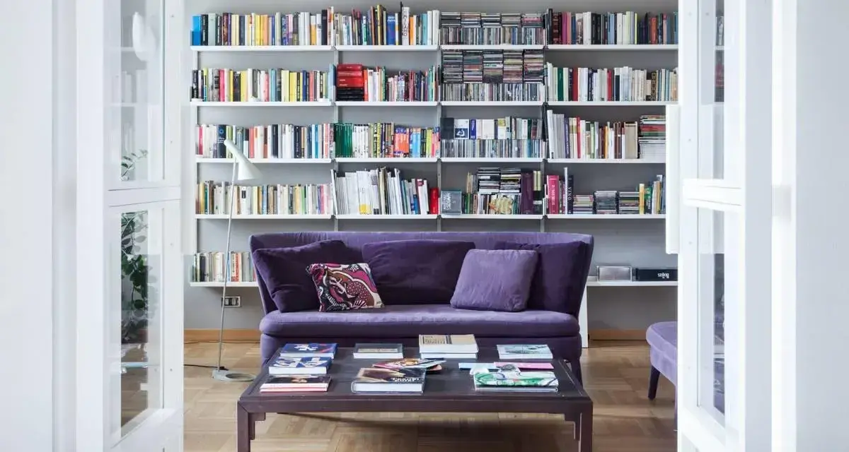 Un divano viola accogliente davanti a una libreria bassa piena di libri e CD.