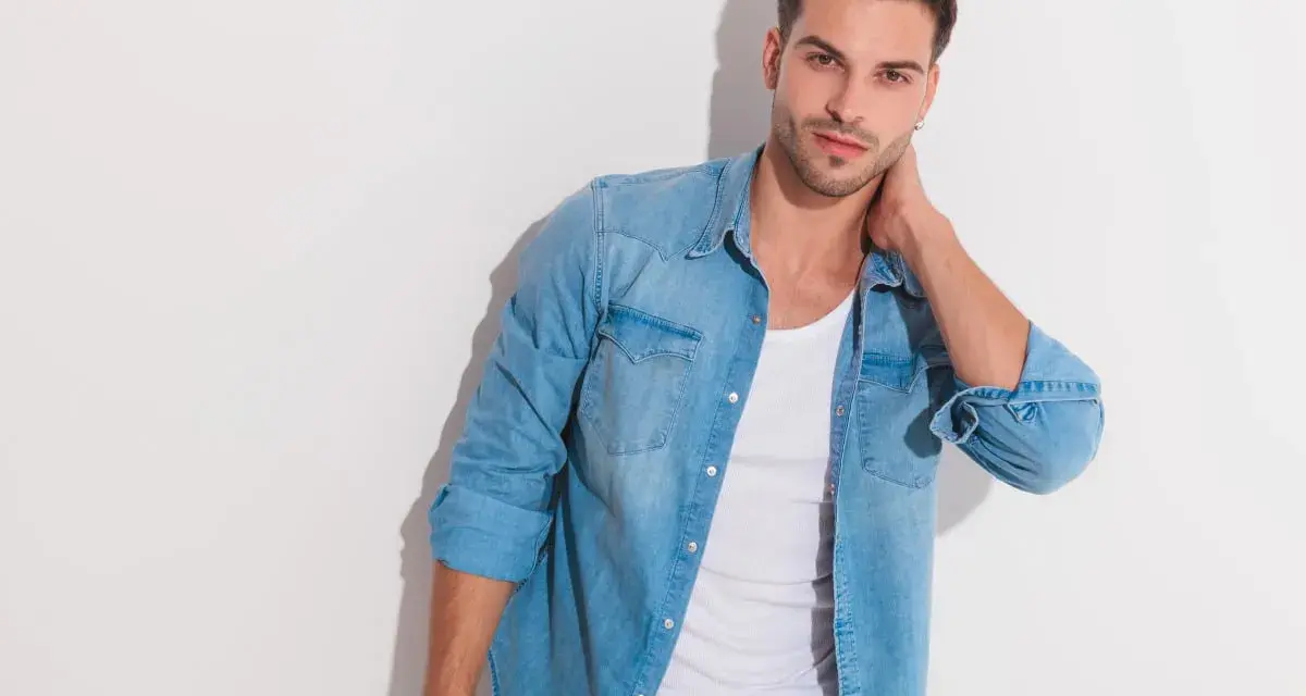 Uomo con un outfit camicia jeans, maglietta bianca e jeans.