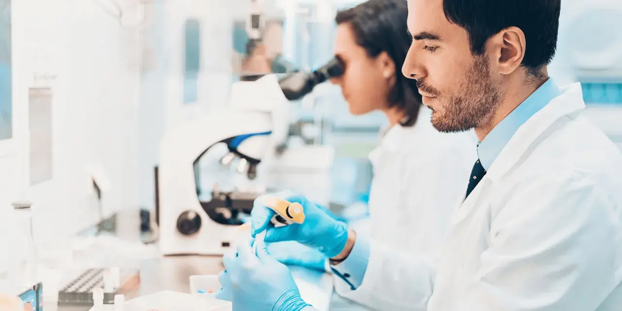 Ricerca di offerte di lavoro tecnico di laboratorio biomedico: due scienziati lavorano con provette e microscopio in un laboratorio moderno.