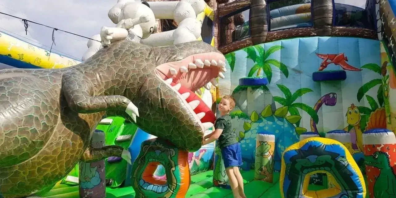 Chłopiec skacze na dmuchanym dinozaurze. Wspaniała atrakcja dla dzieci, jedno z wielu **ciekawe miejsca do 100 km od Katowic**.
