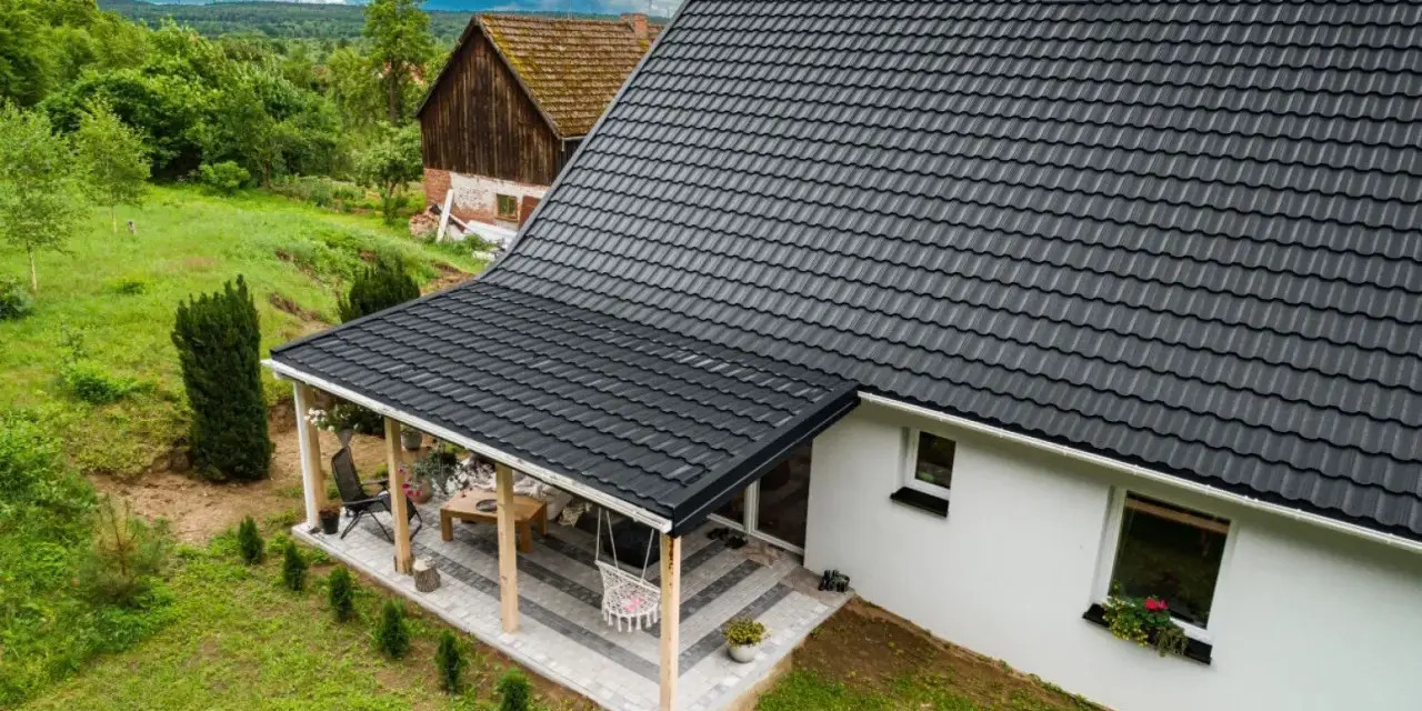Nowy, czarny dach z blachodachówki nad tarasem i domem. Wymiana dachu zakończona sukcesem, dom zyskał nowy, nowoczesny wygląd.