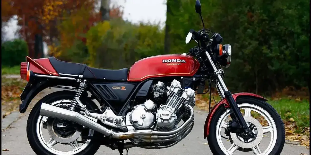 Klasyczny czerwony motocykl Honda CBX 1000 z lat 80. stoi na drodze, otoczony jesienną zielenią i opadłymi liśćmi.