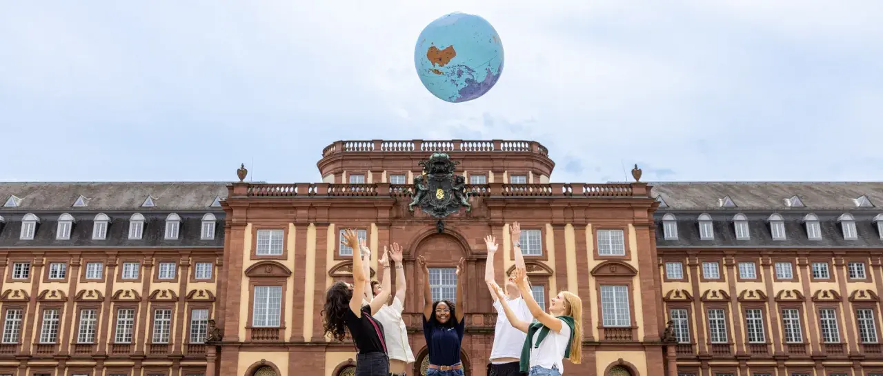 Studierende werfen einen Globus in die Luft vor dem Gebäude des akademischen Auslandsamtes.