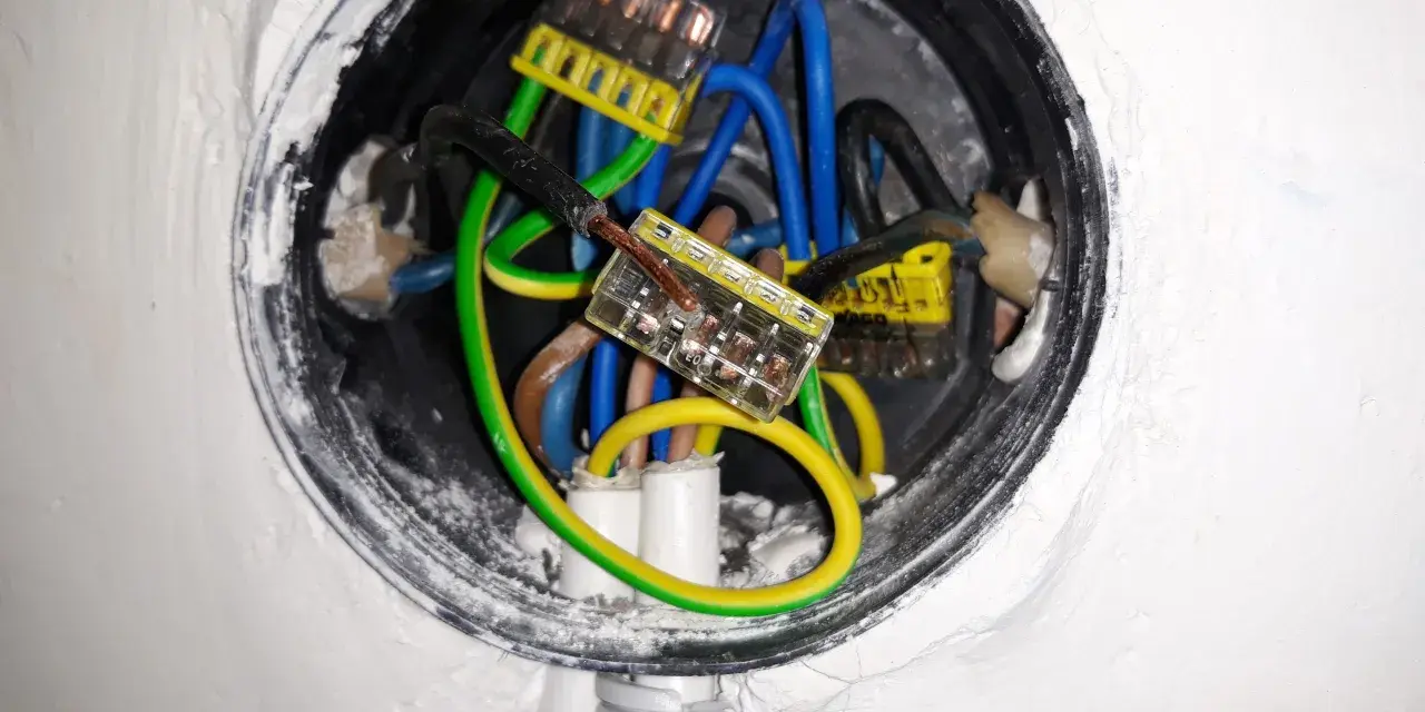 Wnętrze puszki elektrycznej z przewodami: niebieskim, zielono-żółtym i brązowym, połączonymi złączkami. Trwa zerowanie gniazdka.