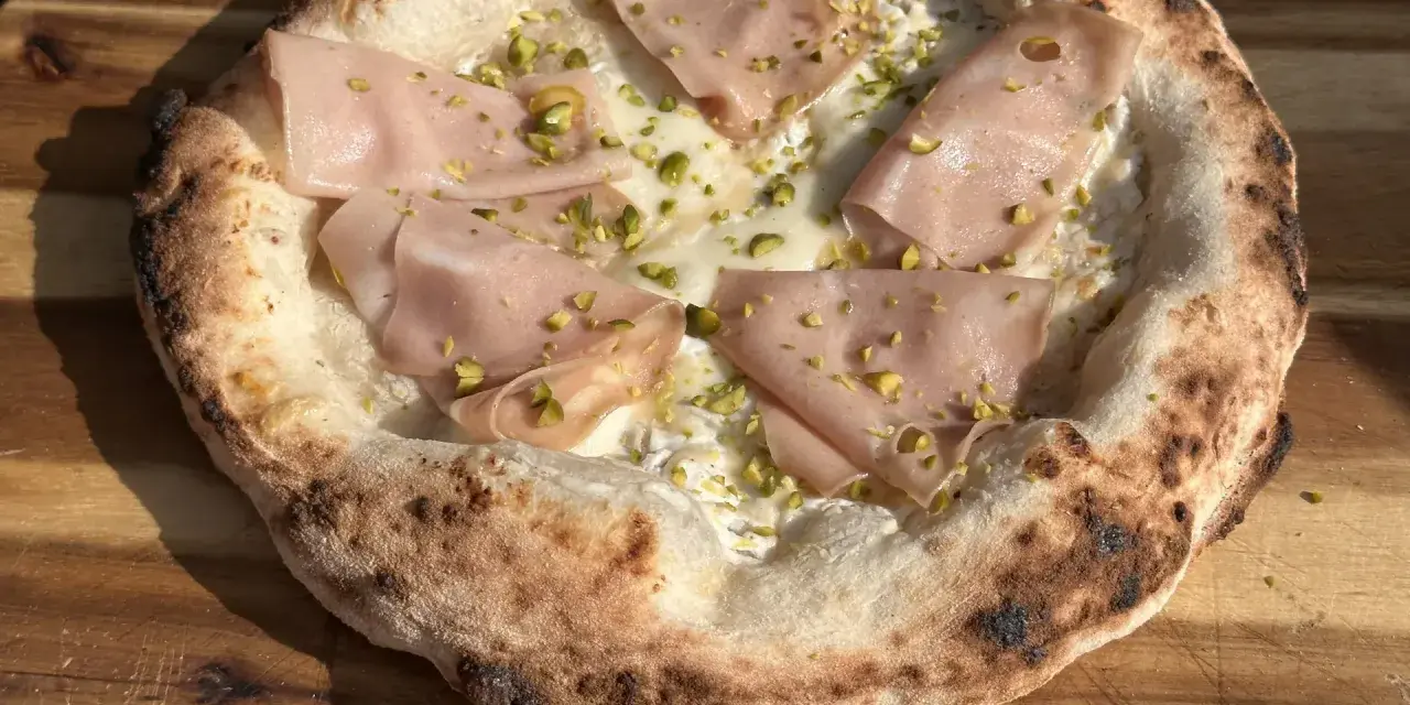 Pizza mit Mortadella und Pistazien auf luftigem pizzateig mit hefe. Der Rand ist knusprig und leicht verbrannt.