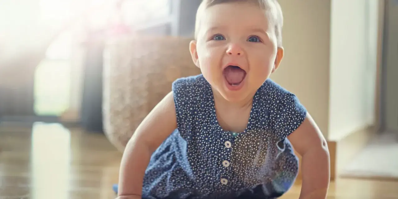 Ein fröhliches Baby hebt Arme und Beine in Bauchlage, bereit zum Krabbeln.