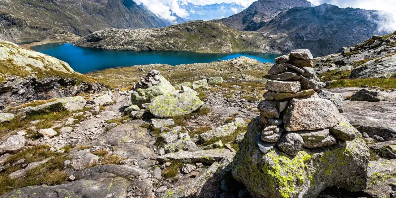 Berglandschaft mit blauem See und Steinmännchen, die den Weg zu den Spronser Seen weisen.