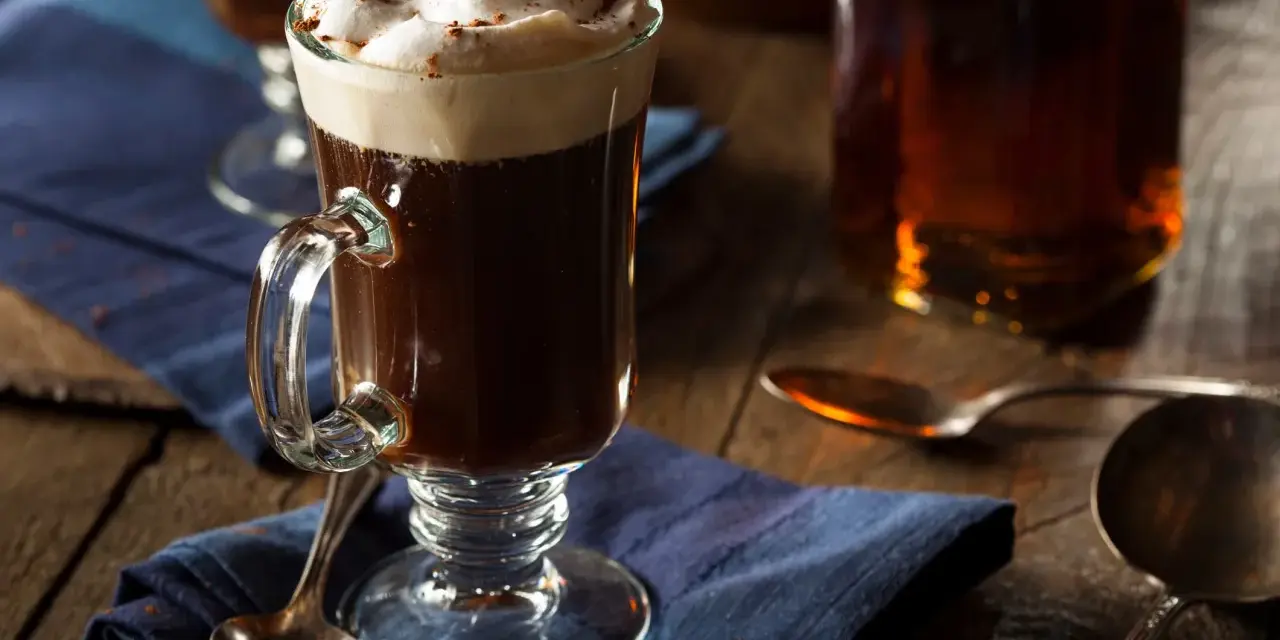 En värmande irish coffee med vispad grädde och kanel på en blå duk.