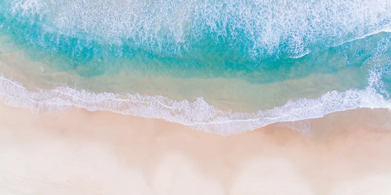 Vue aérienne d'une photo à la plage, avec des vagues turquoise déferlant sur le sable doré.