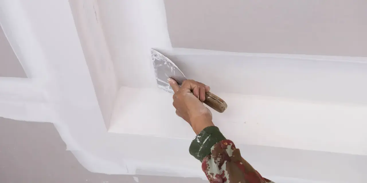 Mano con espátula aplica masilla para pegar escayola rota en el techo.