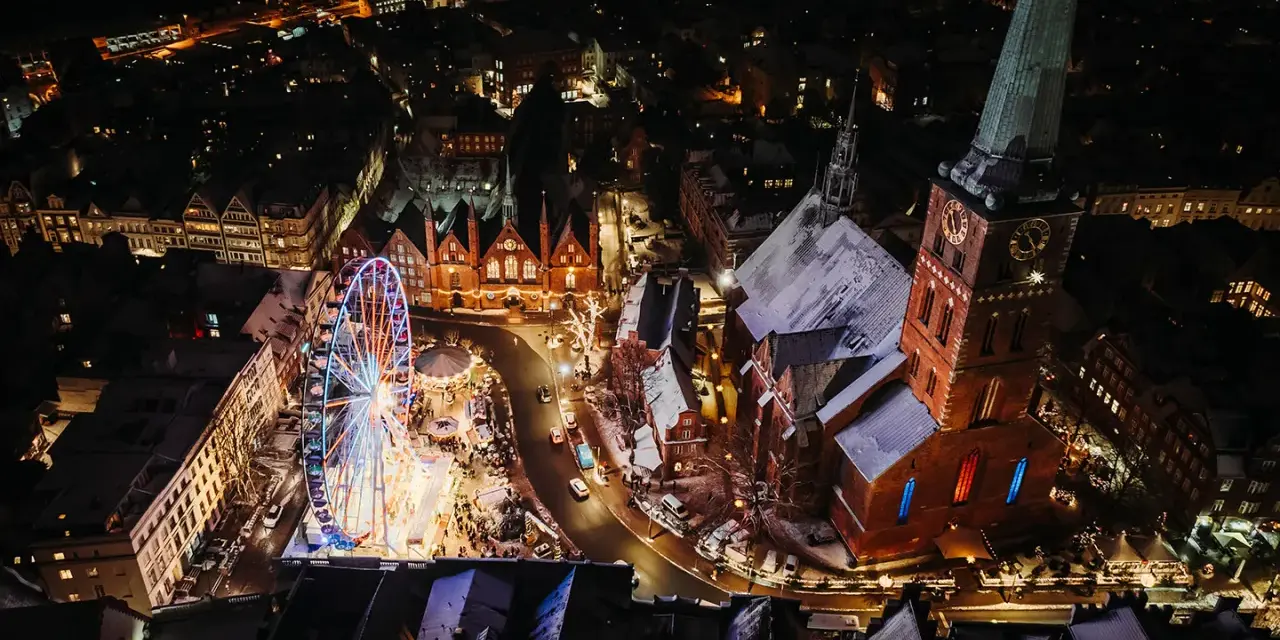 Lichterglanz auf dem Weihnachtsmarkt Schleswig-Holstein: Ein Riesenrad dreht sich neben einer Kirche, während Schneeflocken fallen.