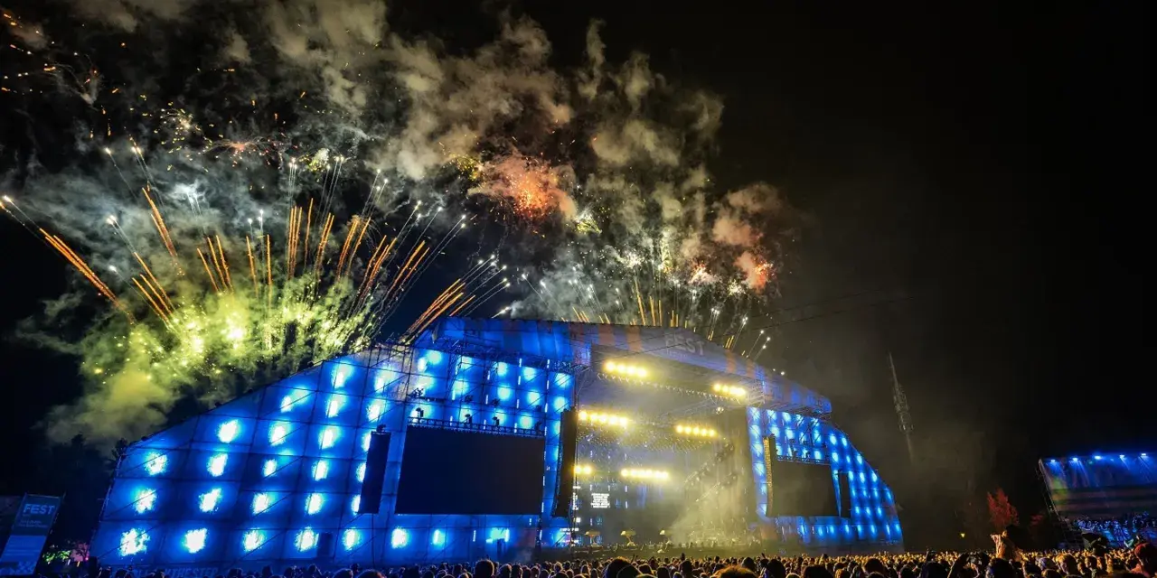 Nocny koncert z fajerwerkami nad sceną. Tłum ludzi podziwia widowisko, a nad nimi rozbłyskują kolorowe petardy.