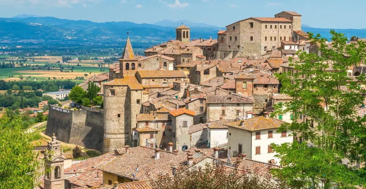 Borgo medievale con tetti in cotto e una torre campanaria, incastonato tra dolci colline verdi. Un luogo che evoca il fascino del **passo dello spino**.