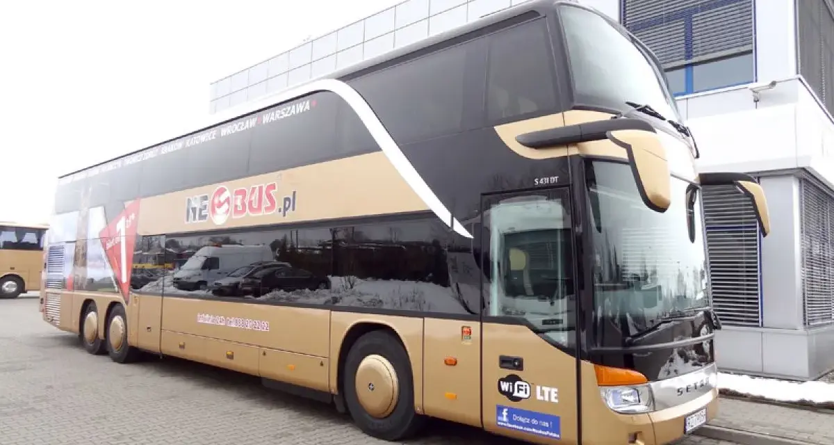 Złoty dwupiętrowy autokar Neobus.pl zaparkowany przed budynkiem.