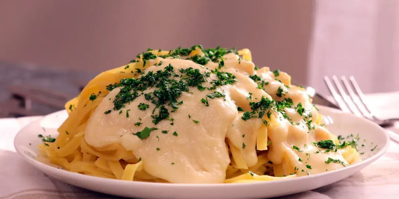 Pasta Alfredo cremosa con perejil picado en un plato blanco.