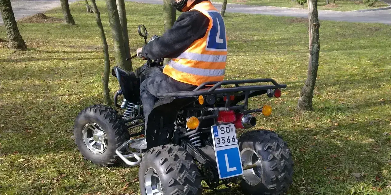 Mężczyzna w kasku i kamizelce odblaskowej siedzi na quadzie z literą L. Zastanawiasz się, jakie prawo jazdy na quada jest potrzebne?