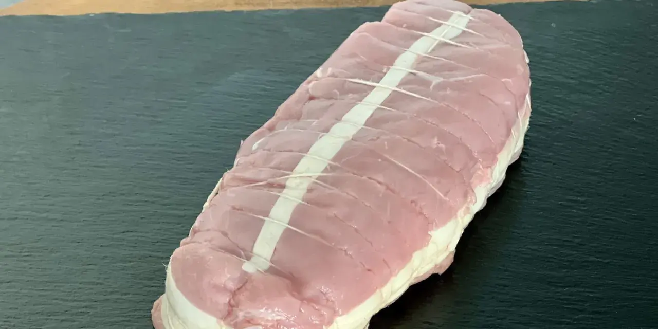 Rôti de veau cru ficelé, prêt à cuire, sur une planche sombre.