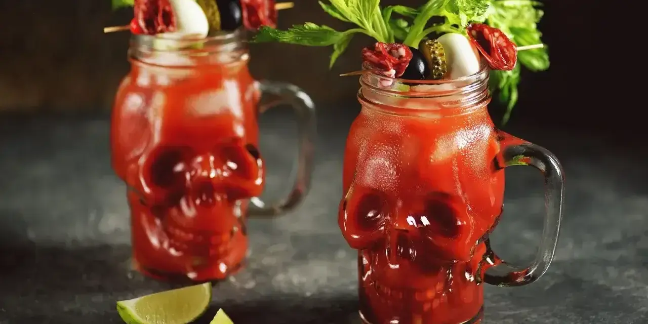 Dwa krwawe drinki ze spirytusem w szklankach w kształcie czaszek, udekorowane łodygami selera, oliwkami i plasterkami salami.