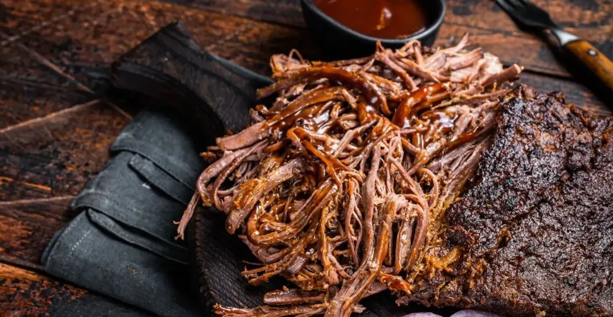 Soczysta, aromatyczna szarpana wołowina, polana sosem BBQ, podana z krążkami cebuli na drewnianej desce. Idealna na grilla.