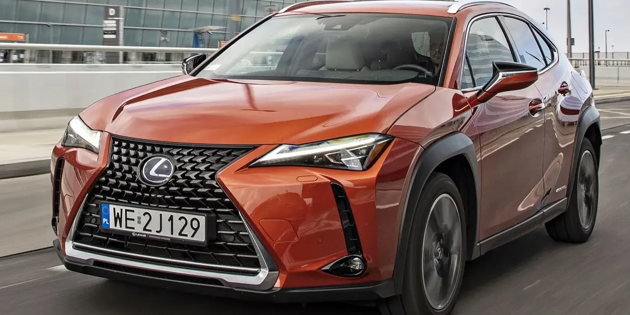 Pomarańczowy Lexus UX 250h w ruchu miejskim, z nowoczesnym grillem i reflektorami LED.