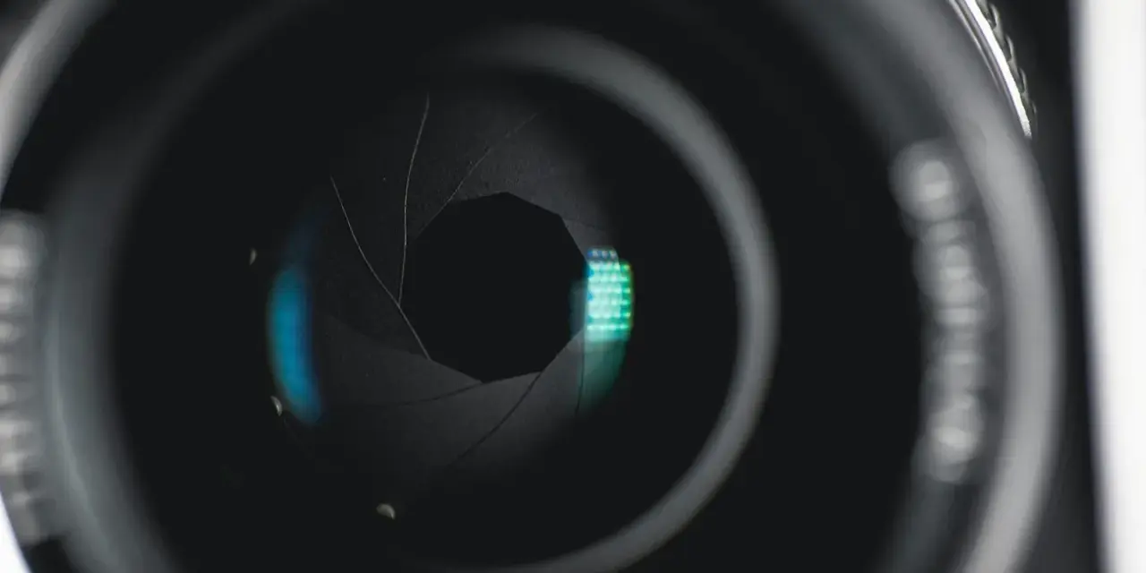 Ouverture d'objectif de caméra, diaphragme réglé sur f 2.8, révélant des reflets bleus et verts.