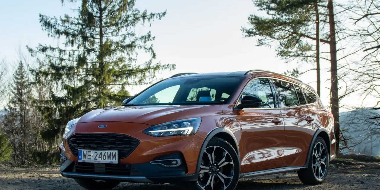 Pomarańczowy Ford Focus kombi na tle drzew i nieba.