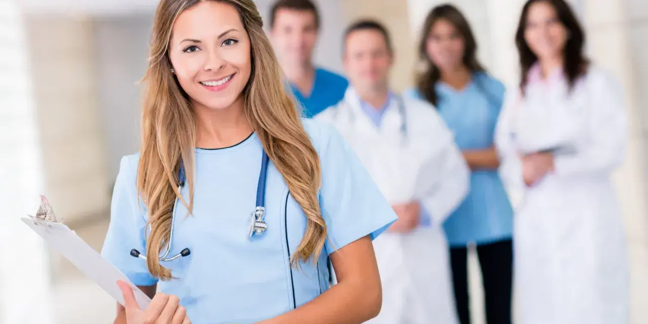 Uśmiechnięta pielęgniarka psychiatryczna z zespołem medycznym w tle. Trzyma tablicę z dokumentami.