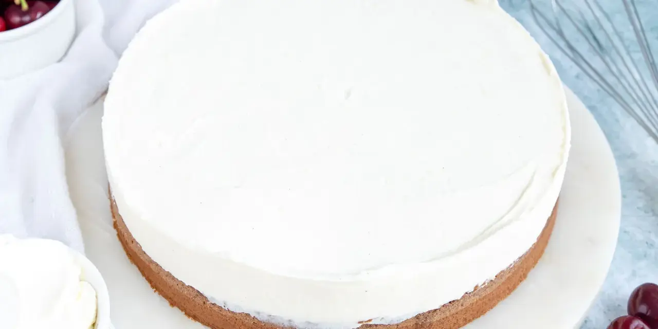 Ein köstlicher Kuchen mit Mascarpone-Creme, garniert mit frischen Kirschen und einem Schneebesen daneben.