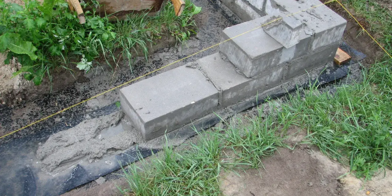 Fundamenty z betonu i bloczków, częściowo zalane, otoczone trawą. Pytanie, czy można zostawić odkryte fundamenty na zimę, jest tu kluczowe.