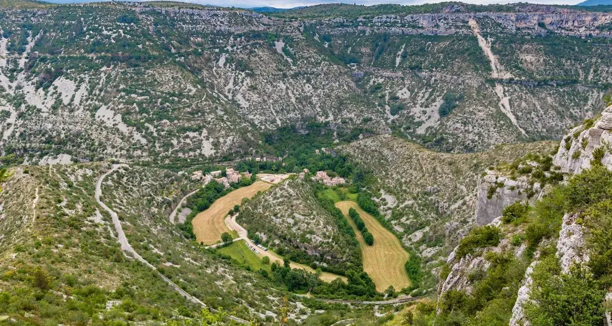 Vue aérienne du cirque de Navacelles, un méandre de rivière creusé dans un paysage de garrigue et de falaises calcaires, avec un village niché au fond.