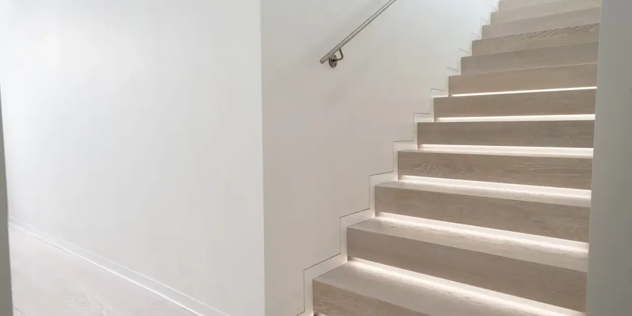 Scala moderna con gradini in legno illuminati e un discreto profilo battiscopa filo muro che ne esalta la pulizia delle linee.