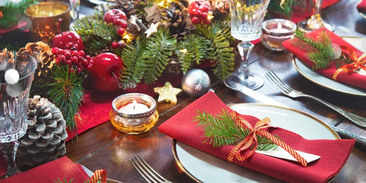 Vackert dukat julbord med röda servetter, granris, äpplen, kottar och ljus. Här ser du vad man har på ett julbord för att skapa julstämning.