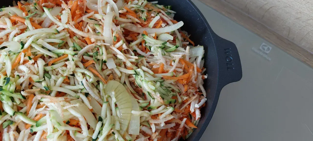 Start przygotowania keto ryby po grecku: starta marchewka, cukinia i cebula w naczyniu.
