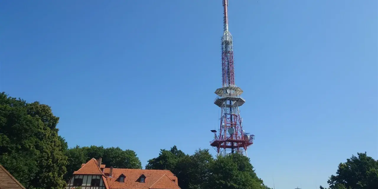 Wieża widokowa na górze Ślęża góruje nad budynkiem schroniska i zielonymi drzewami.