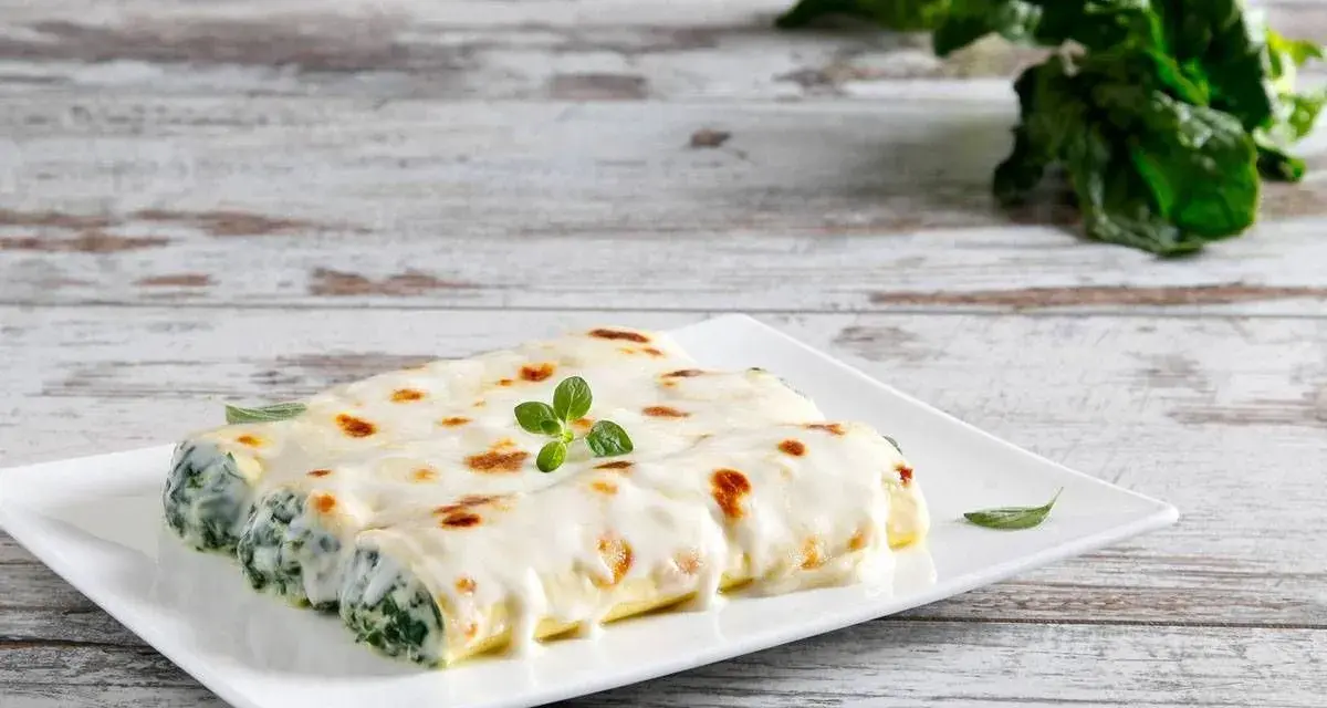 Cannelloni ricotta e spinaci fumanti, ricoperti di besciamella e gratinati, guarniti con un rametto di origano.