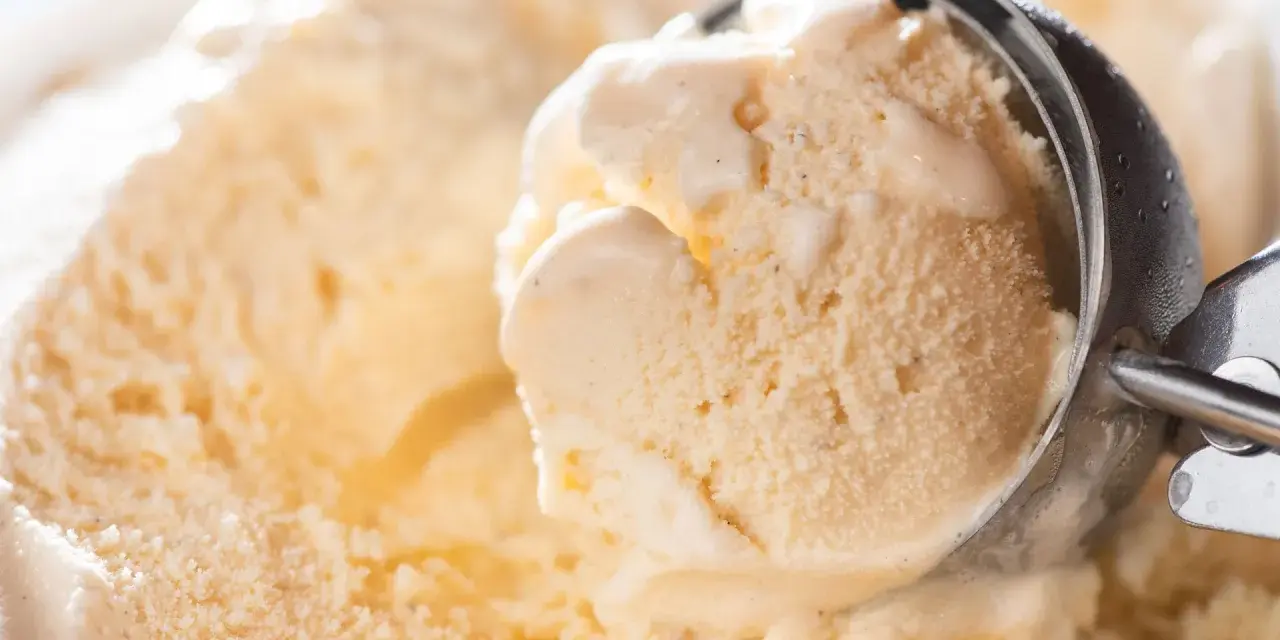 Ein Löffel nimmt eine Kugel cremiges Eis auf. Kleine eiskristalle im eis glitzern im Licht.