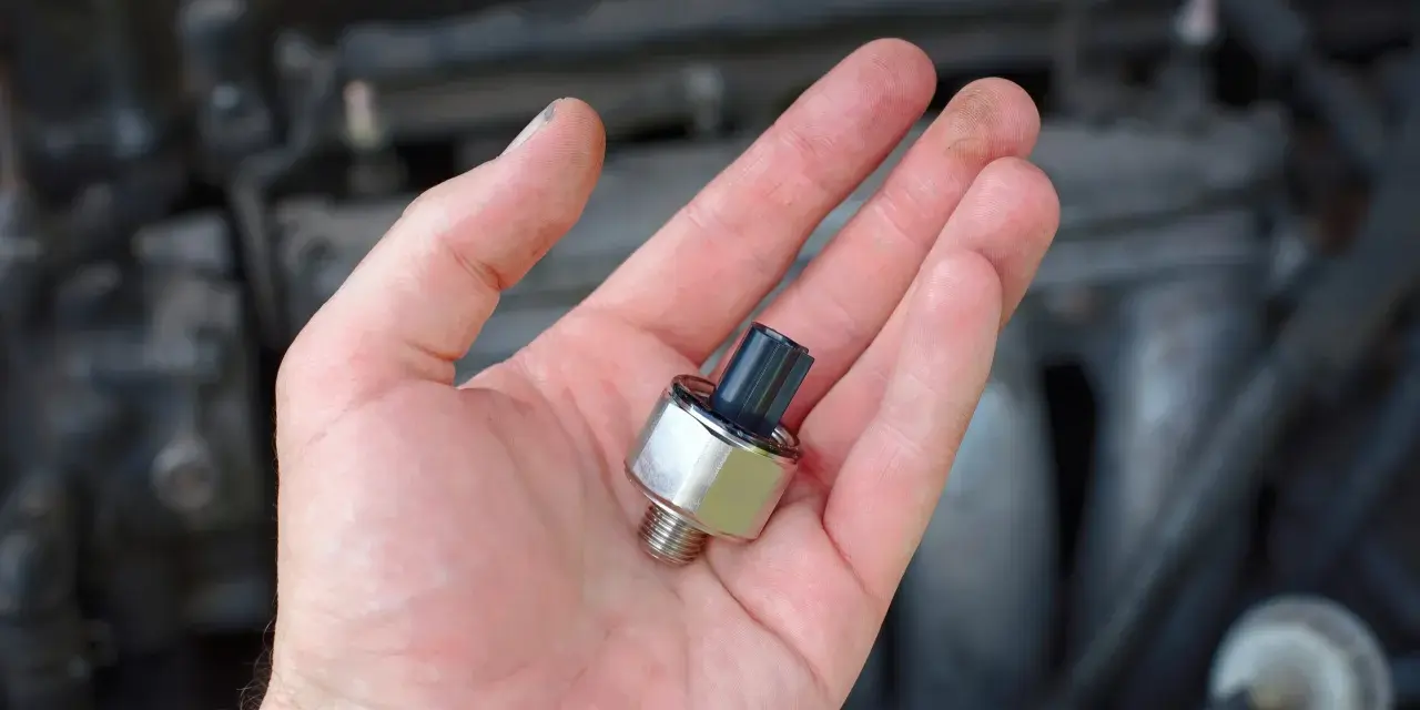 A hand holds a new oil pressure sensor, a potential fix for a p0332 code Chevy Silverado.