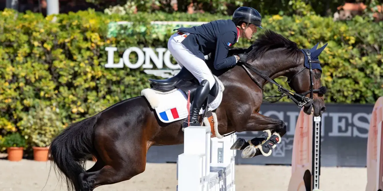 Cavalier français en plein saut lors d'un concours hippique. Le cheval, puissant et concentré, franchit un obstacle blanc.