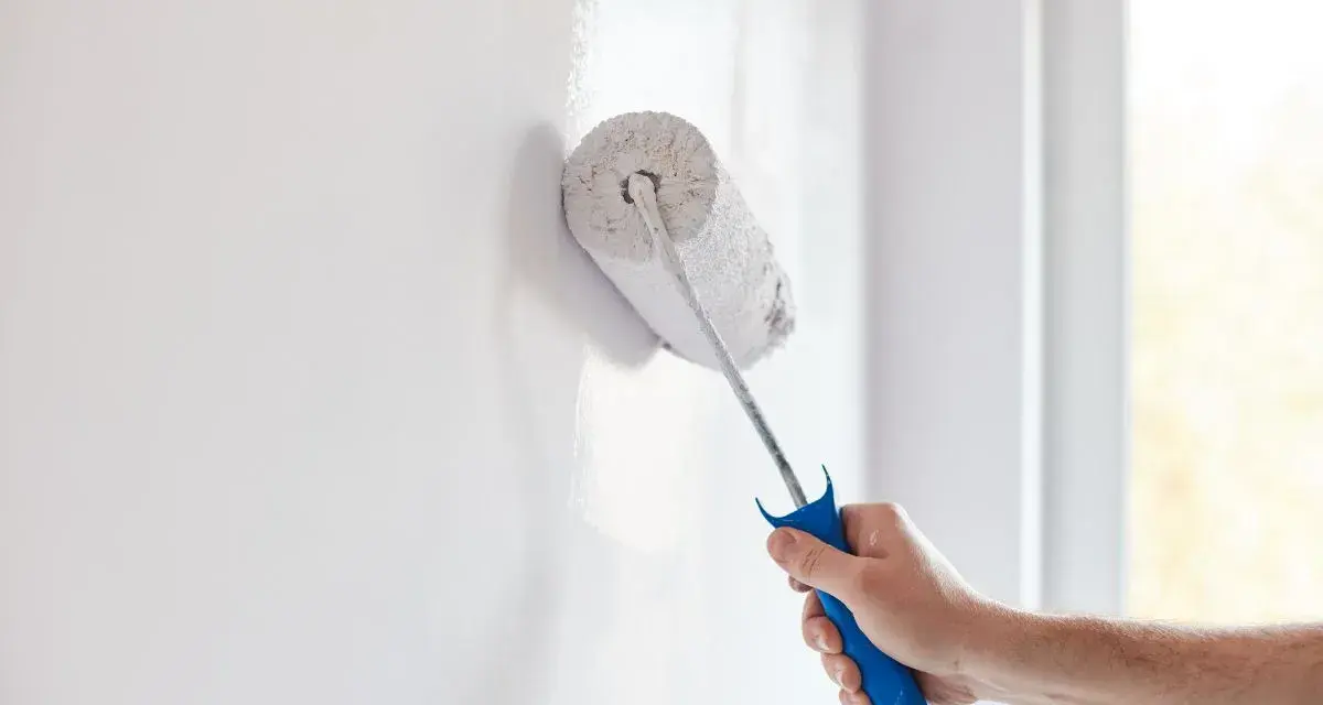 Mano pintando pared blanca con rodillo. Creando diseños de paredes pintadas con cinta para un acabado perfecto.