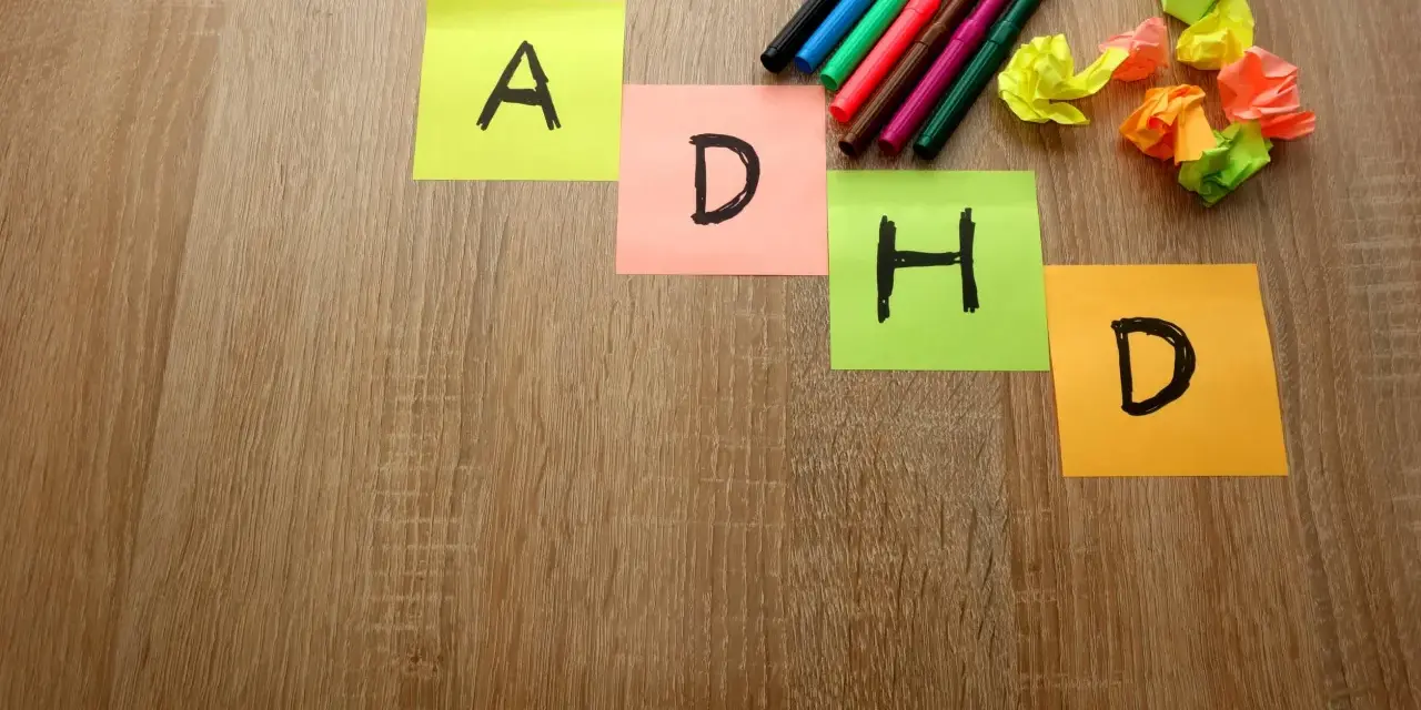 Kolorowe karteczki z literami "A", "D", "H", "D" układają się w napis ADHD. Obok leżą pisaki i pomięte papierki, jakby ktoś próbował znaleźć rozwiązanie, może z pomocą leku Elvanse.
