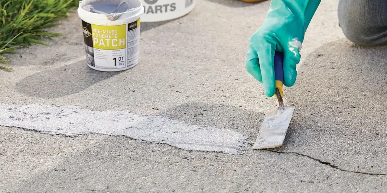 Applying pre-mixed concrete patch to fix cracks in pavement. A gloved hand uses a trowel to smooth the patch.