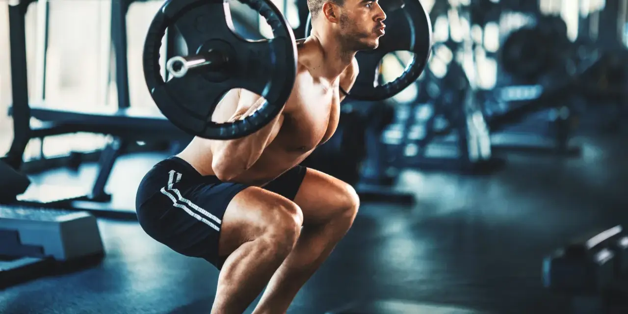 Man gör ett tungt benspark hemma med skivstång på axlarna i ett gym.