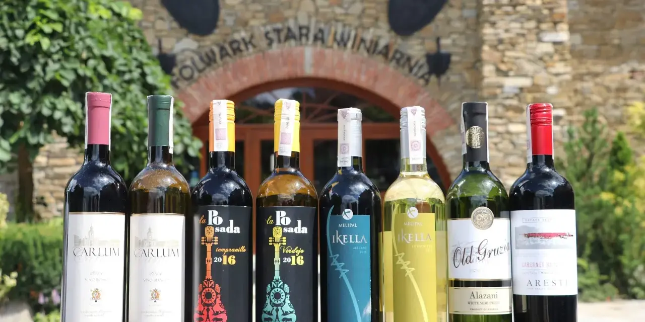 Wybierasz jakie wino na wesele? Rząd butelek z winem czerwonym i białym przed starą winnicą.