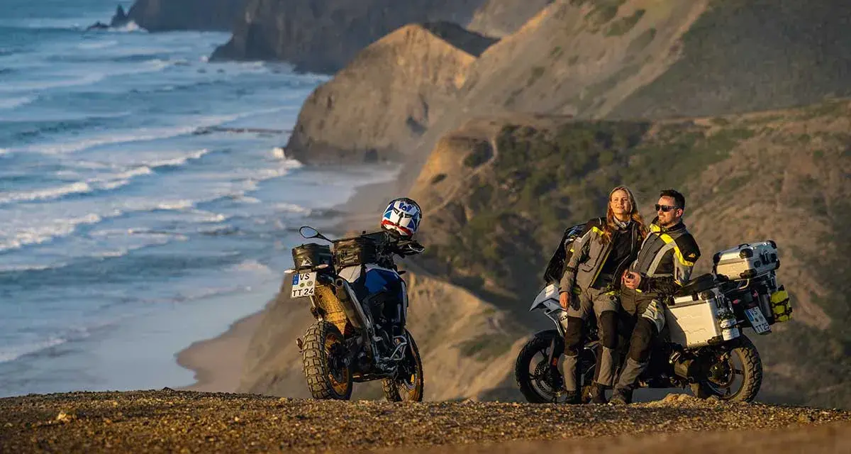 Para motocyklistów odpoczywa na klifie, podziwiając dzikie wybrzeże Algarve. Ich motocykle gotowe do dalszej podróży.